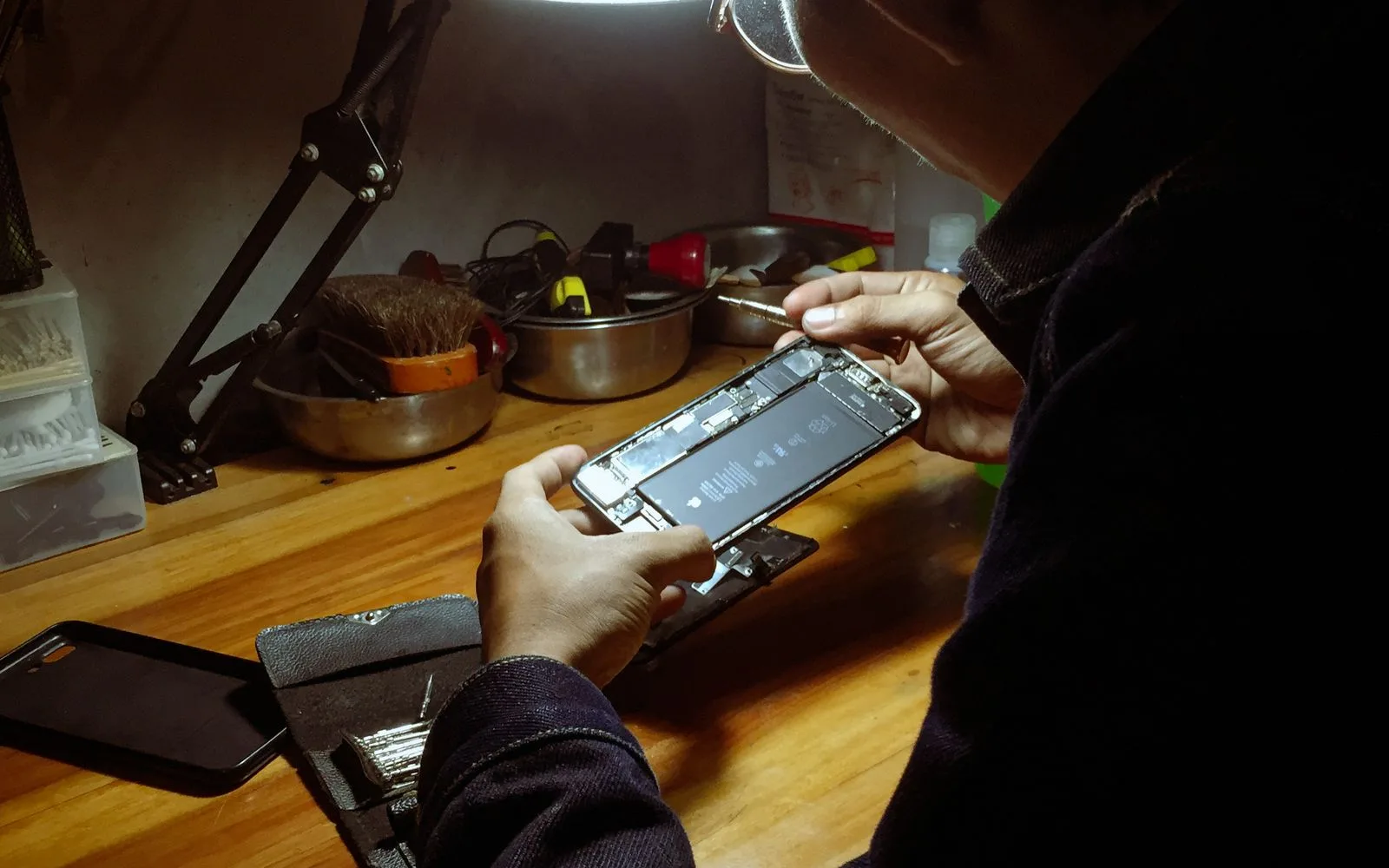 Technician holding an opened iPhone with the battery exposed at a repair bench