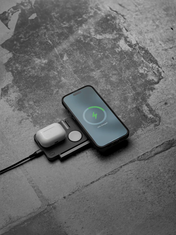 An iPhone charging on a wireless pad beside AirPods and an Apple Watch