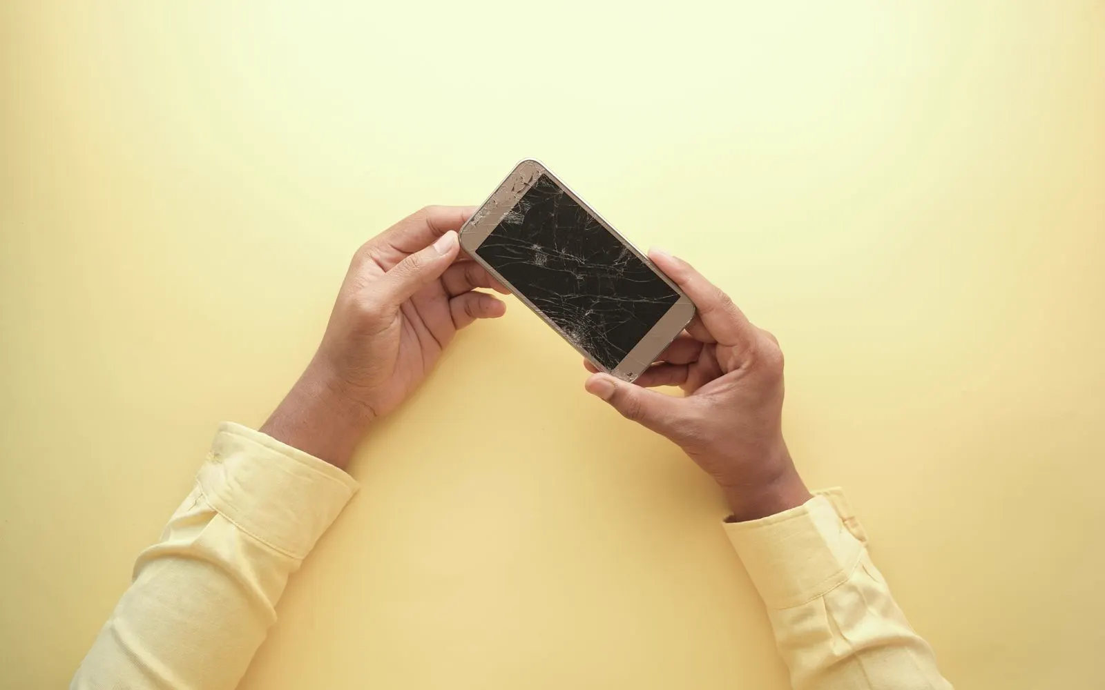 Two hands holding a cracked smartphone, the damage being looked over
