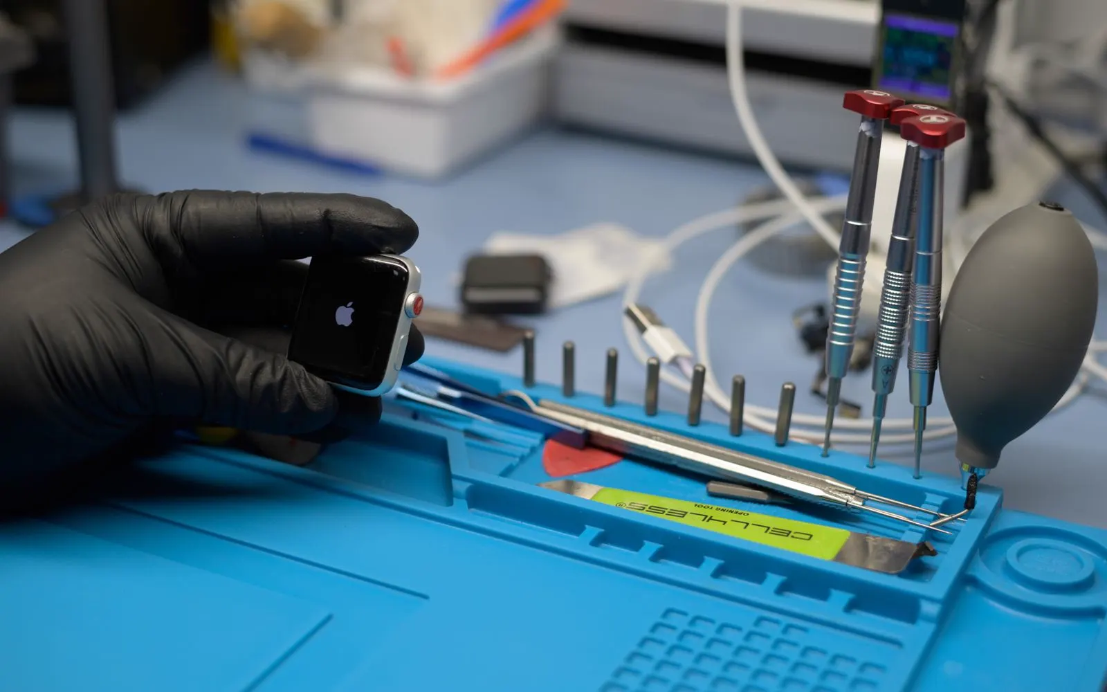 A technician in gloves working on a cell phone at a repair bench, tools laid out beside it