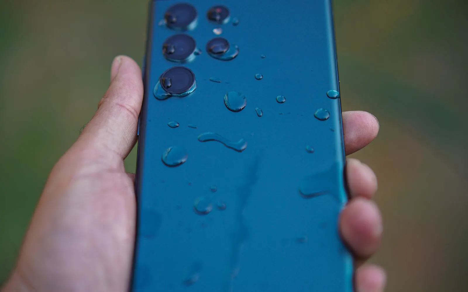 A hand holding a smartphone covered in water droplets outdoors