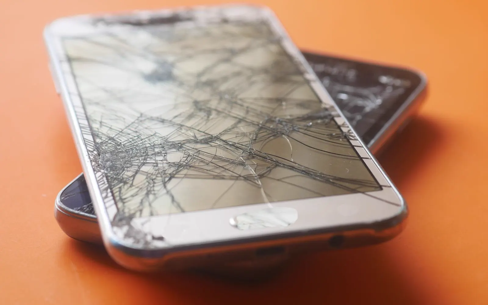 Two damaged smartphones lying on an orange background