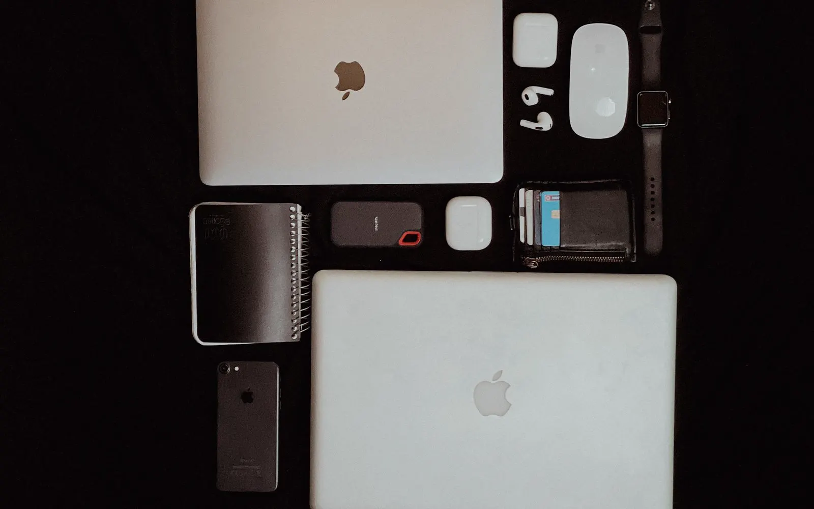 Two MacBooks laid out with an iPhone, earphones, a watch and an external drive