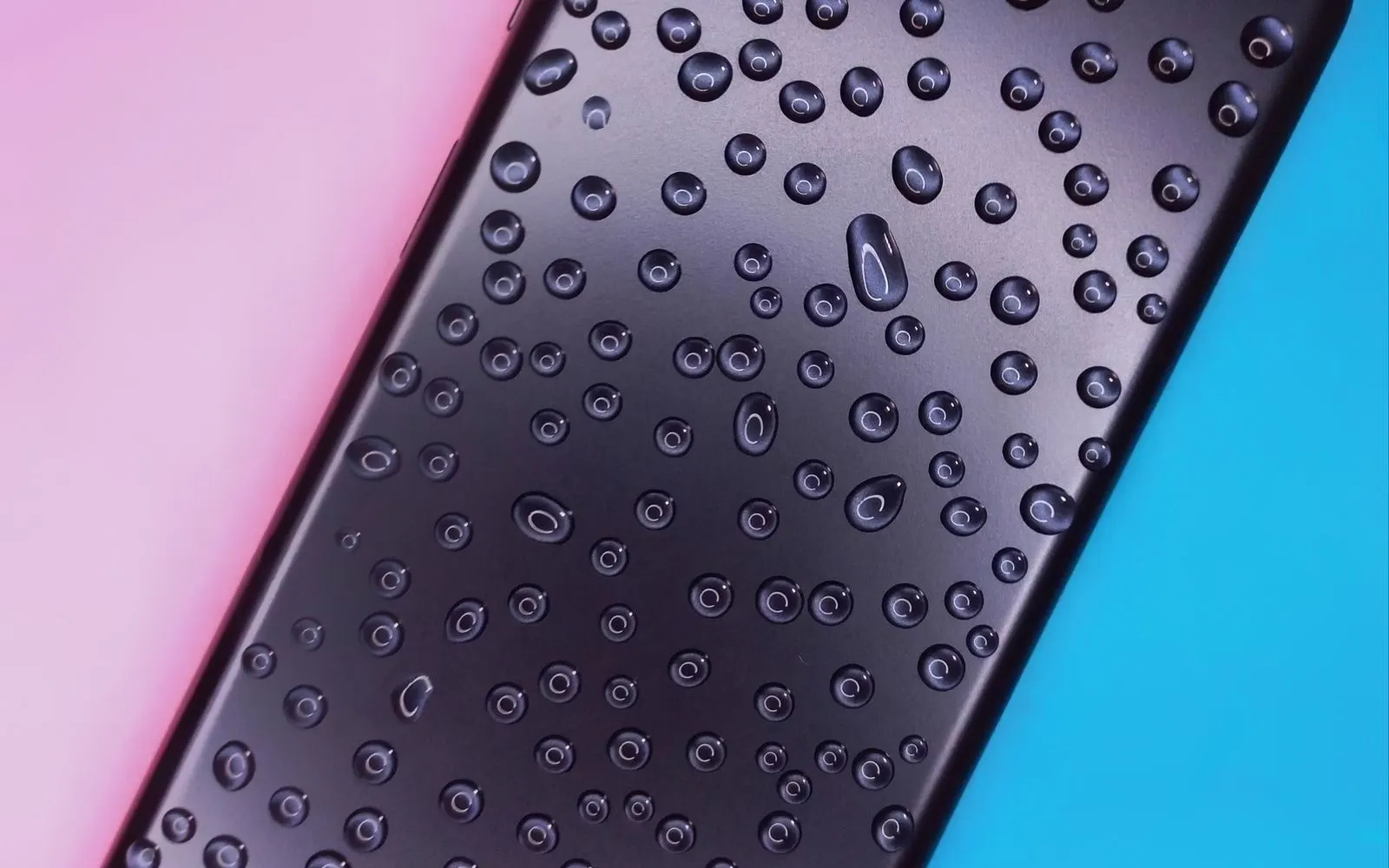 A black smartphone covered in water droplets against a coloured background