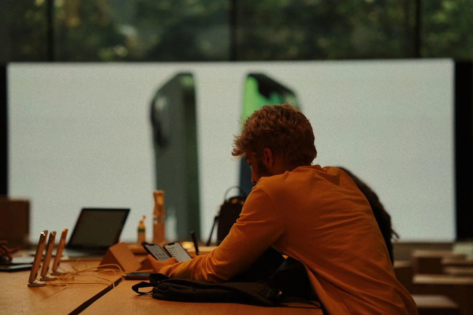 A customer at a device table in a phone store, a tablet and a laptop in front of them