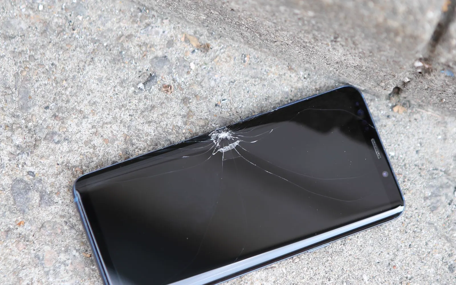 A cracked smartphone lying on concrete pavement