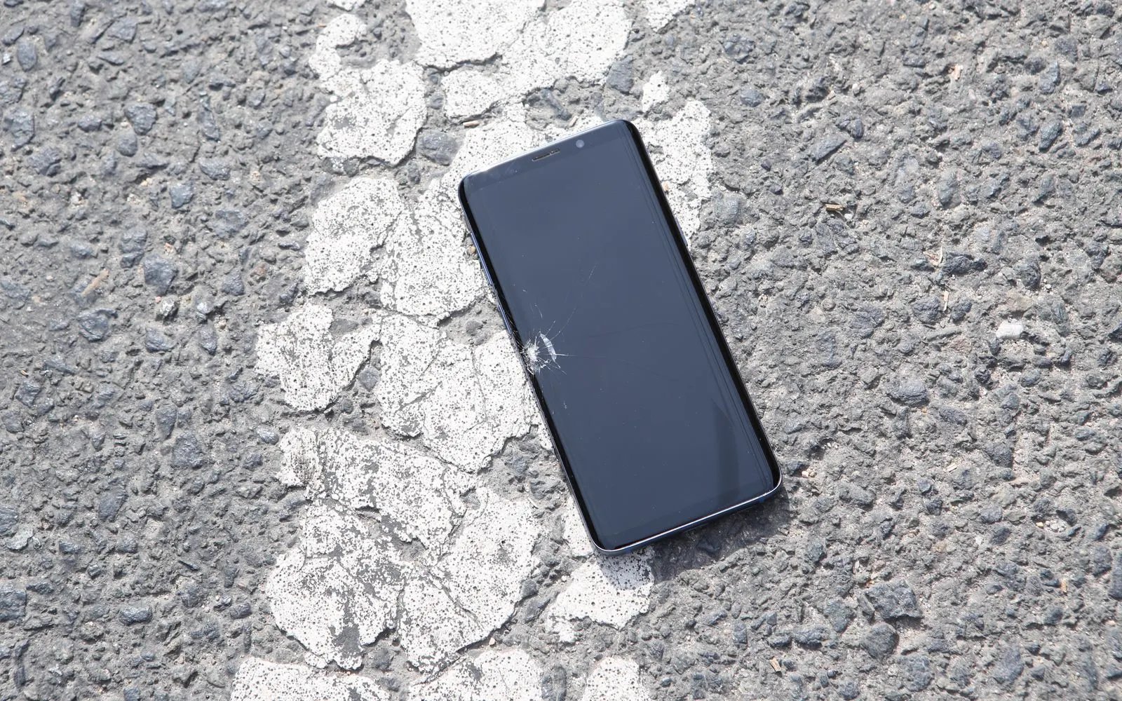 A smartphone with a damaged screen lying face up on asphalt
