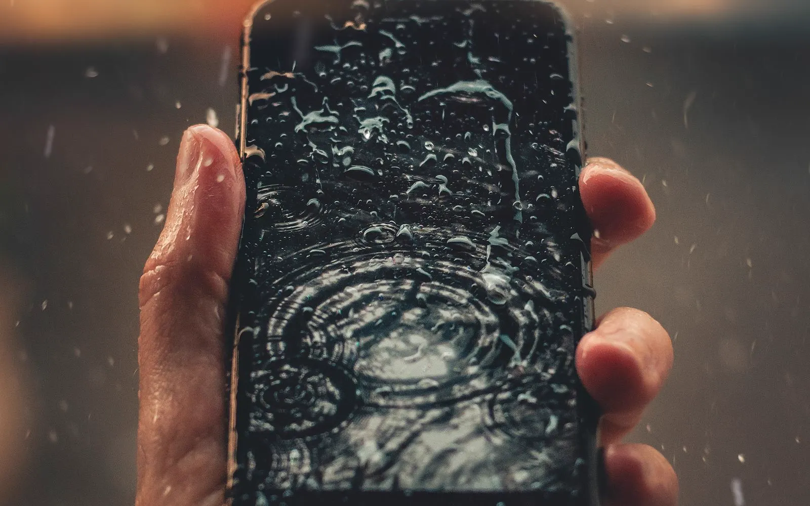 A hand holding a smartphone covered in water droplets