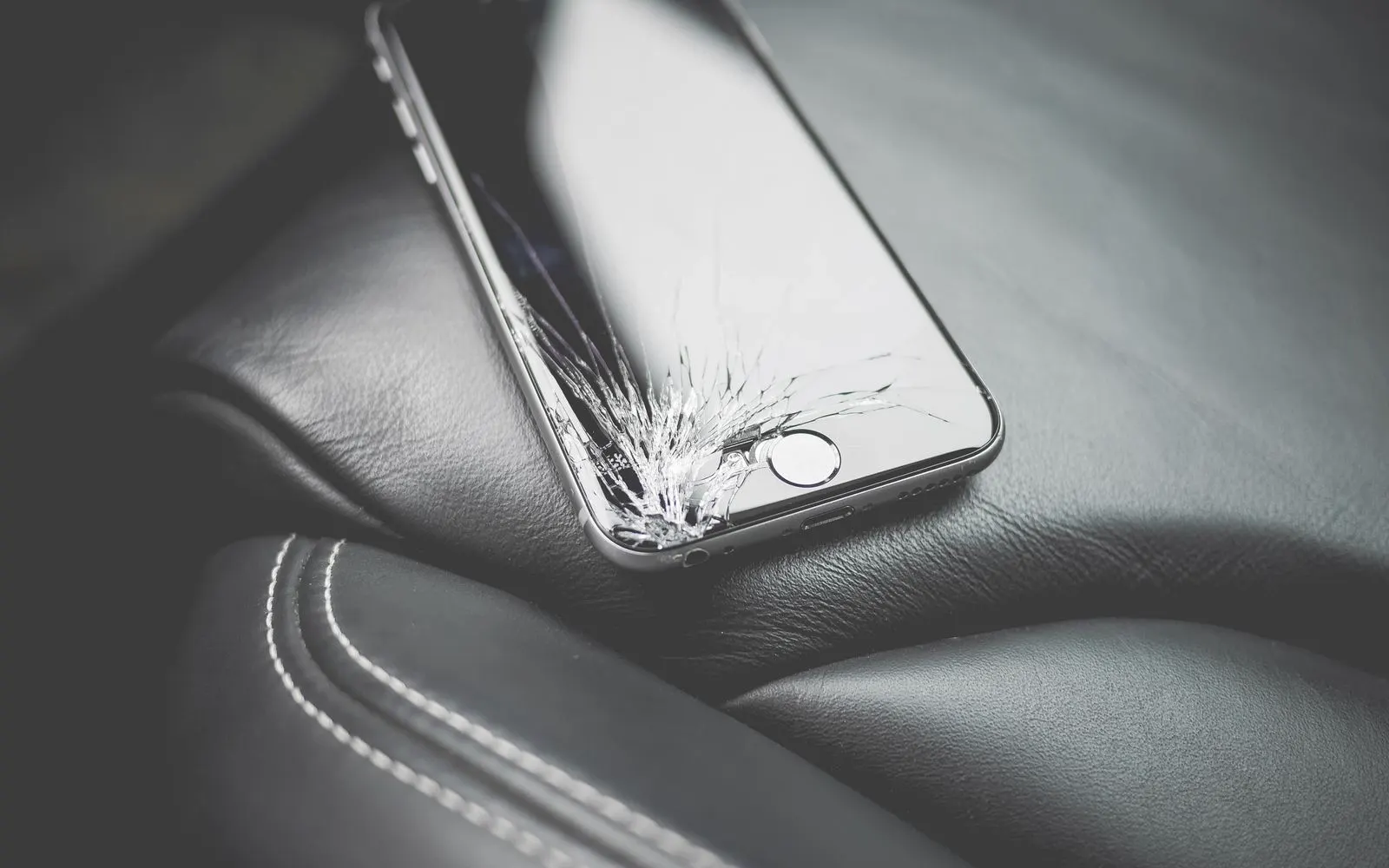 A smartphone with a badly cracked screen lying on a car seat
