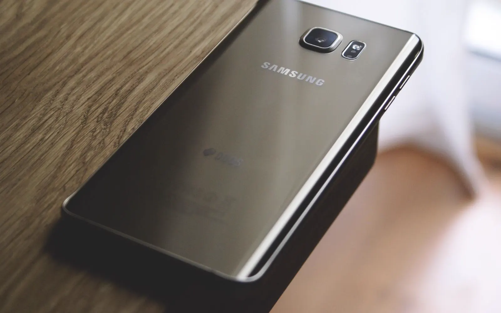 A Samsung phone resting face down on a wooden desk