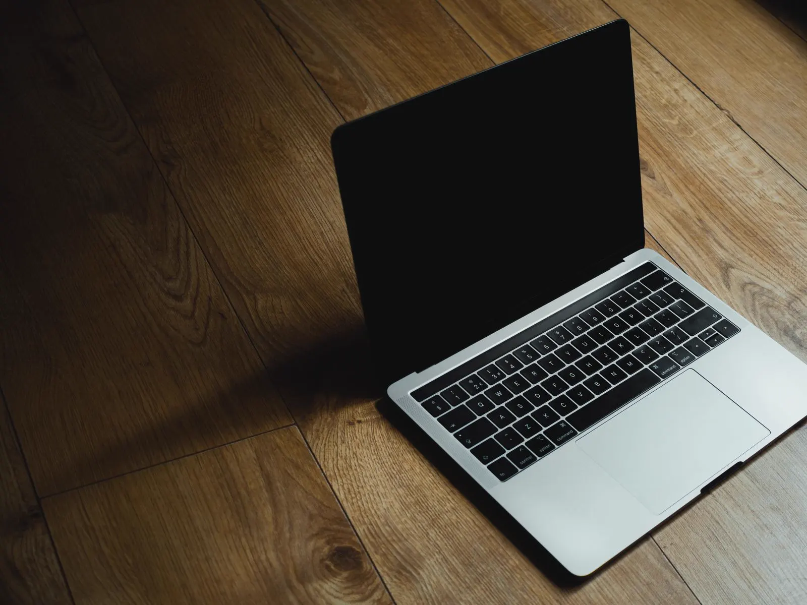 An open MacBook Pro resting on a wooden floor
