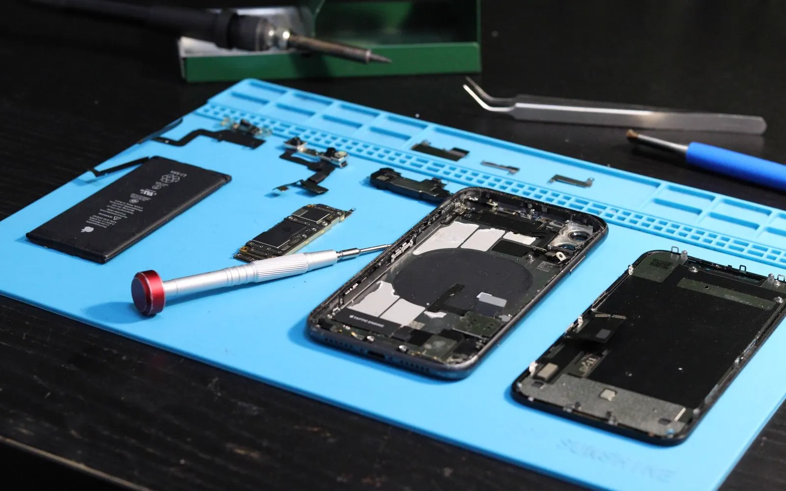 A disassembled smartphone and its battery laid out on a blue repair mat