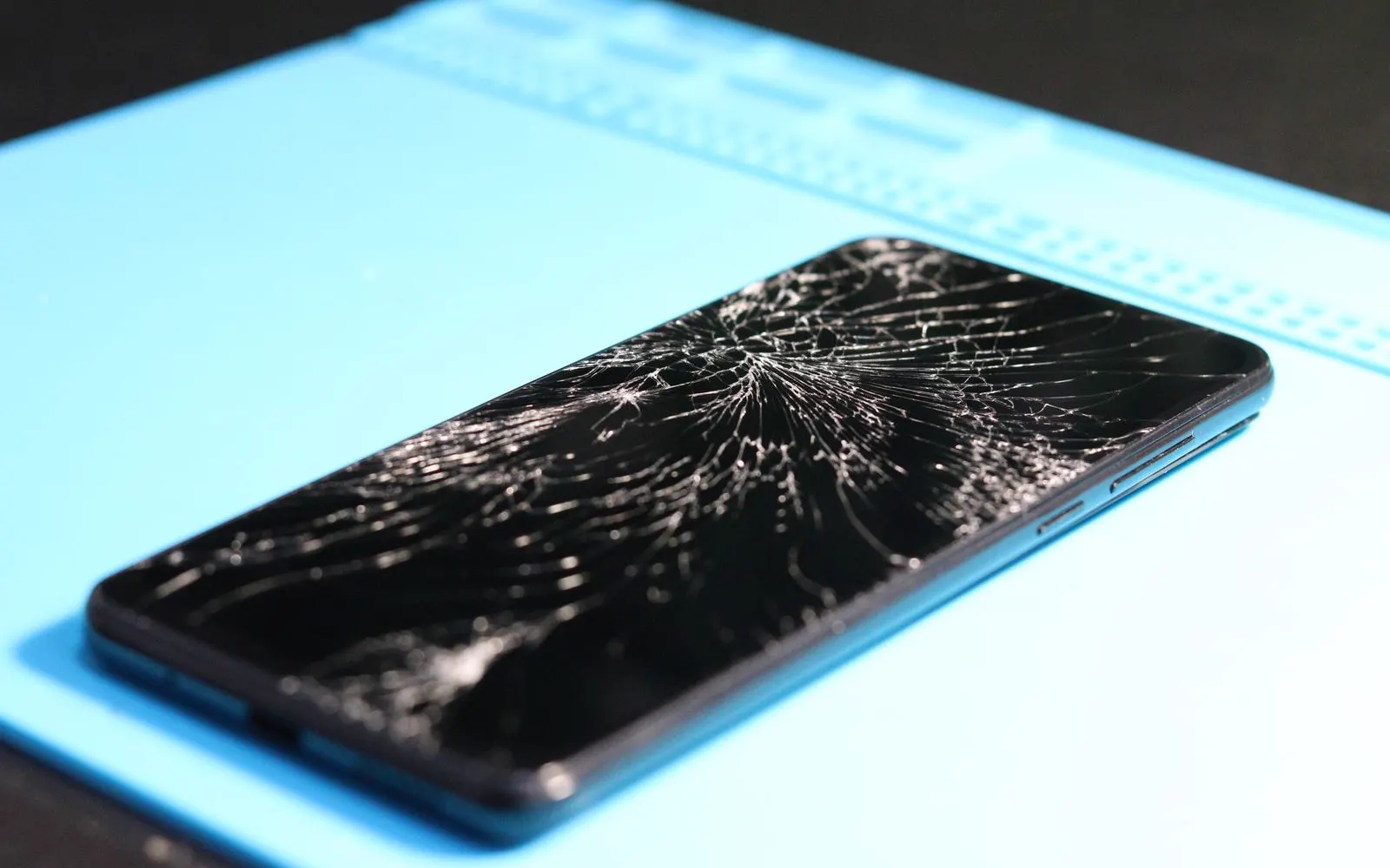 A cracked smartphone screen on a blue repair mat