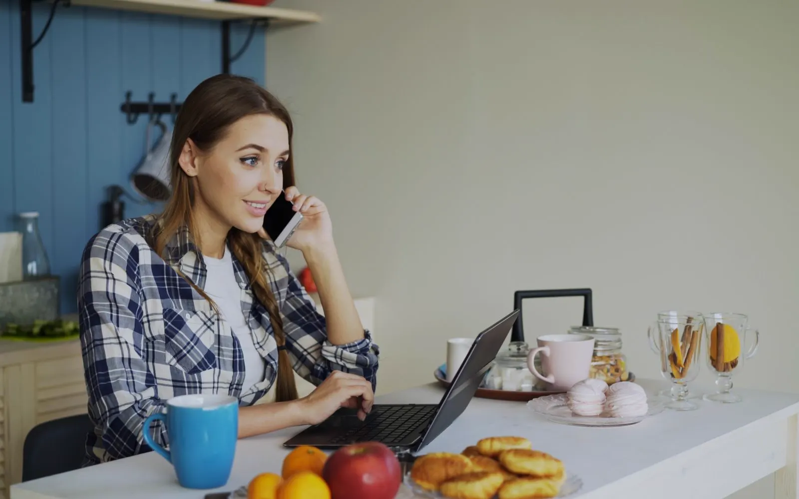 A person on a phone call at a kitchen table with an open laptop in front of them