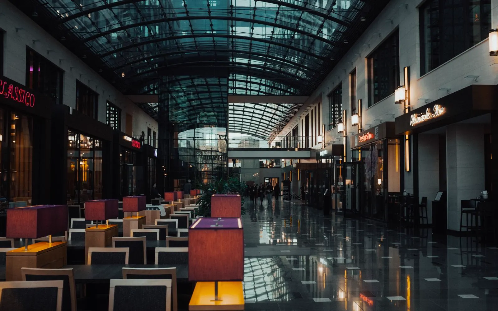 The concourse of a shopping centre running beneath a vaulted glass roof