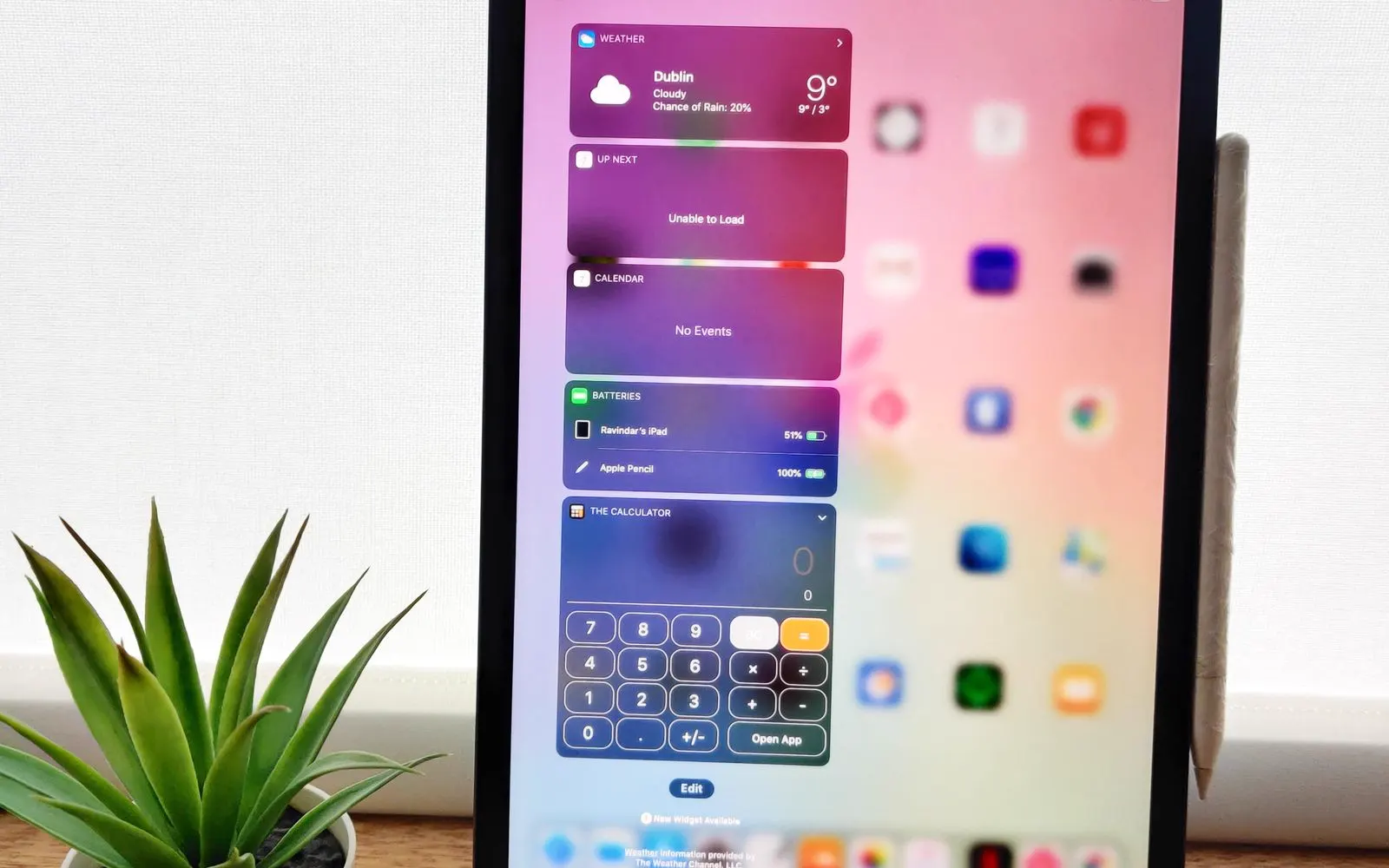 An iPad home screen showing its widgets, stood on a wooden desk