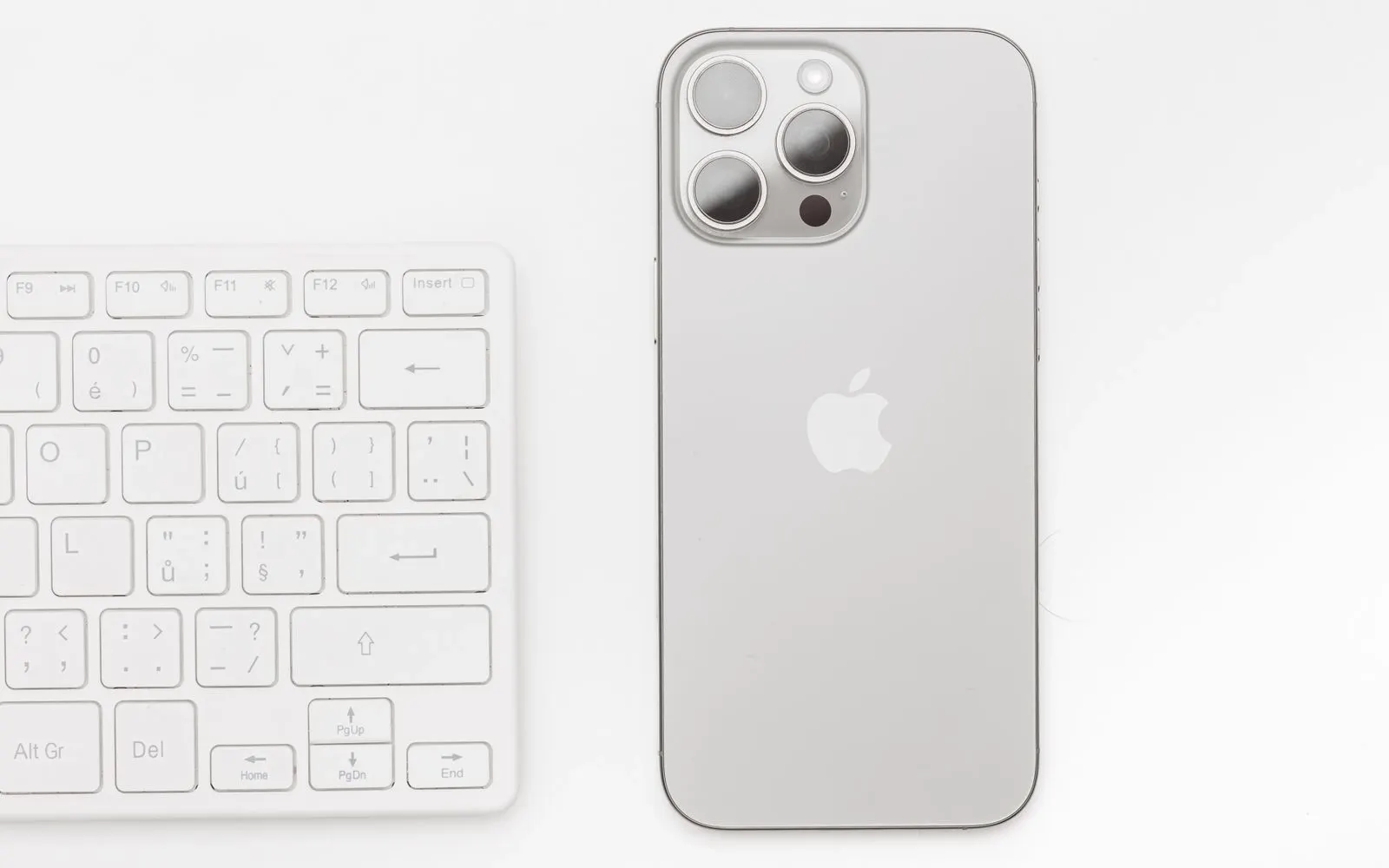 A recent silver iPhone lying beside a keyboard on a white desk