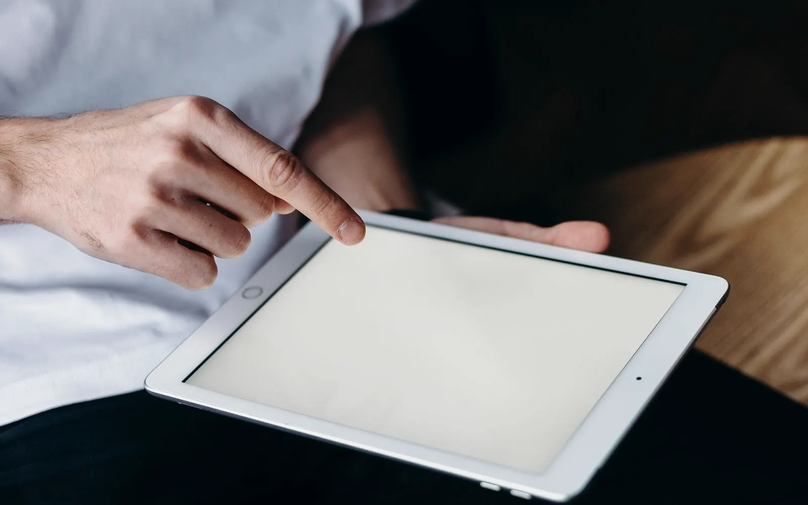 A finger resting on the Home button of a white iPad held on a lap