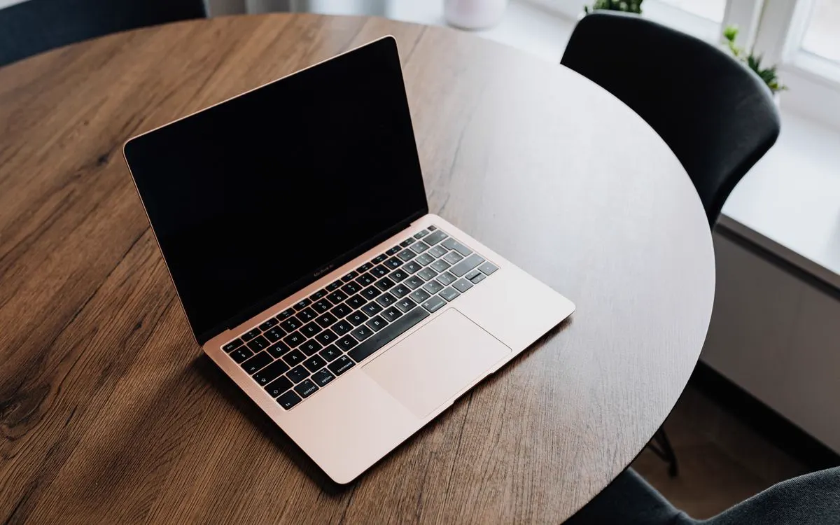 A rose gold MacBook open on a round wooden table