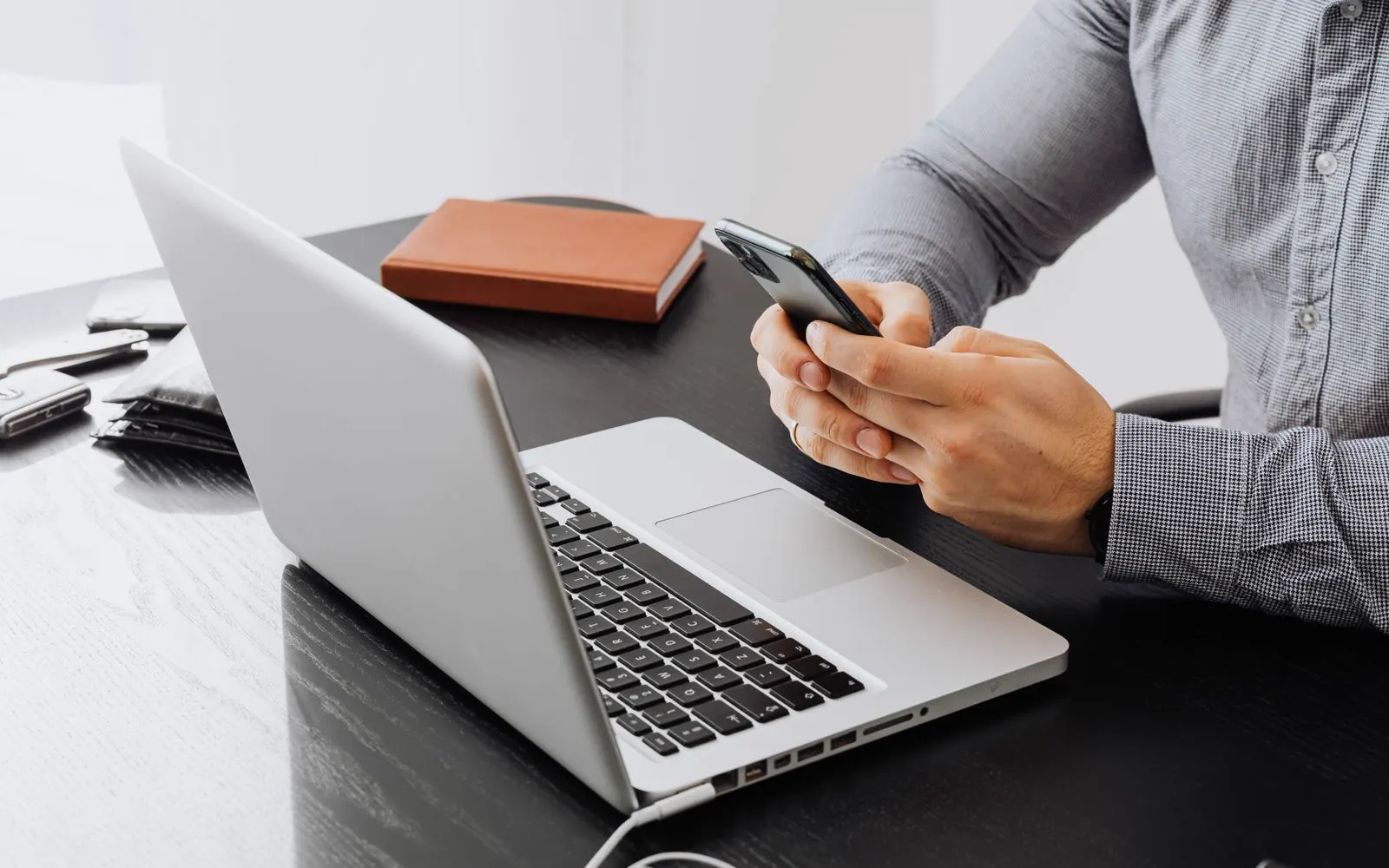 A person using a phone at an office desk beside a laptop