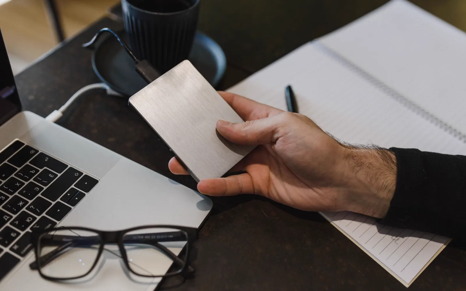 A person holding an external hard drive beside an open laptop