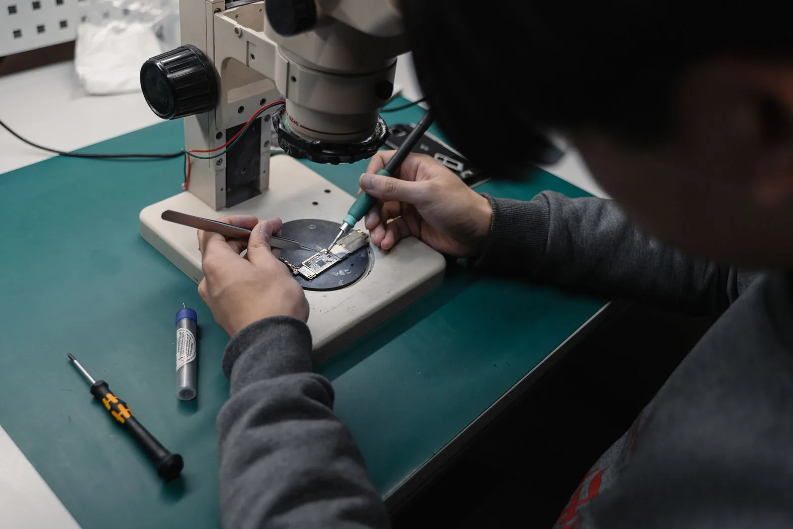A technician working on a phone board under a bench microscope