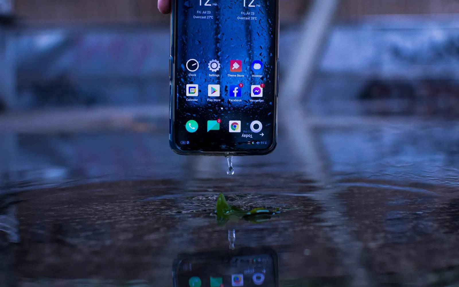 A hand holding a smartphone above a wet reflective pavement