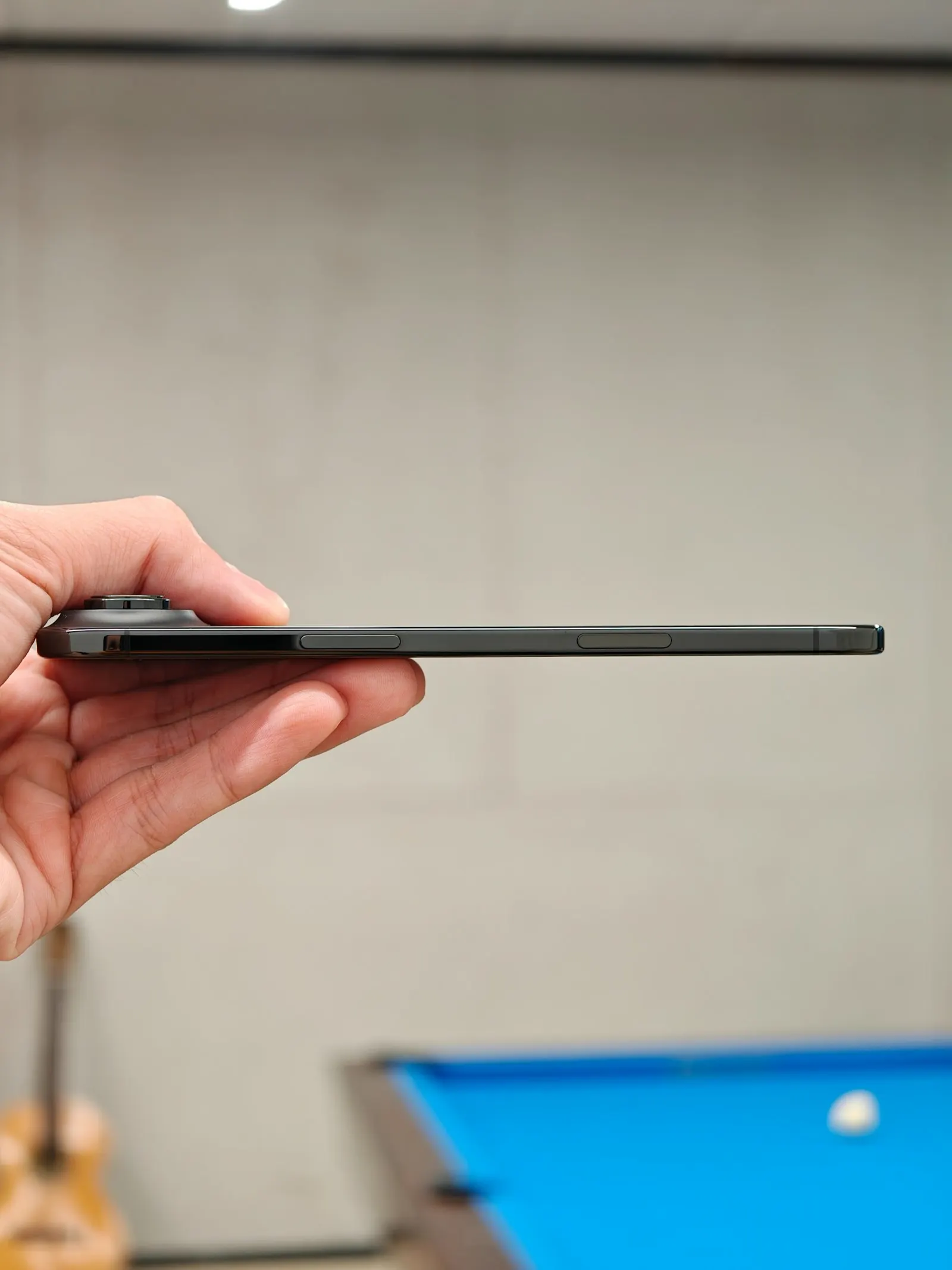 A hand holding a slim, dark smartphone in pristine condition